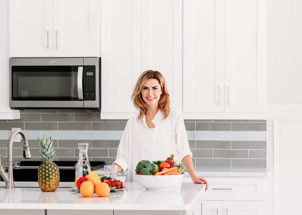 Brand image of dietary coach  standing  in bright kitchen with colorful fruits and vegges on the kitchen island