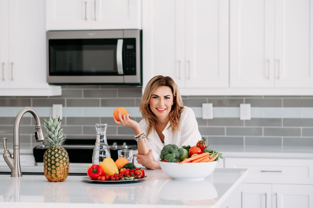 Health and diet coach in her bright white  kitchen with fruit and vegetable on the table