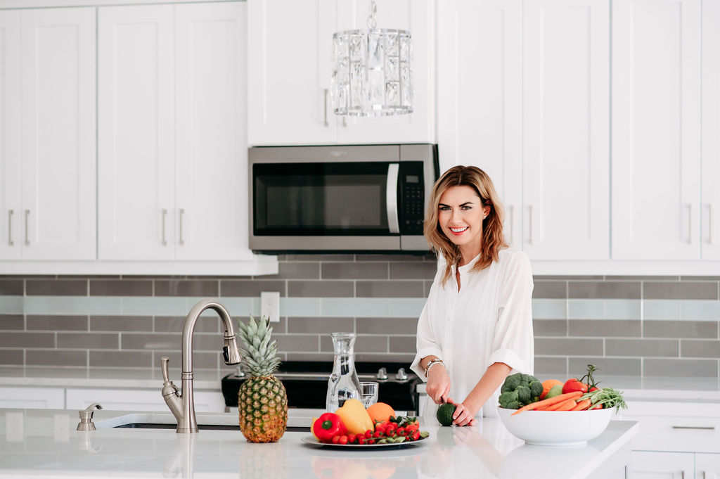 Beautiful women cutting avocado in bright kitchen with colorful fruits and vegges on the kitchen island