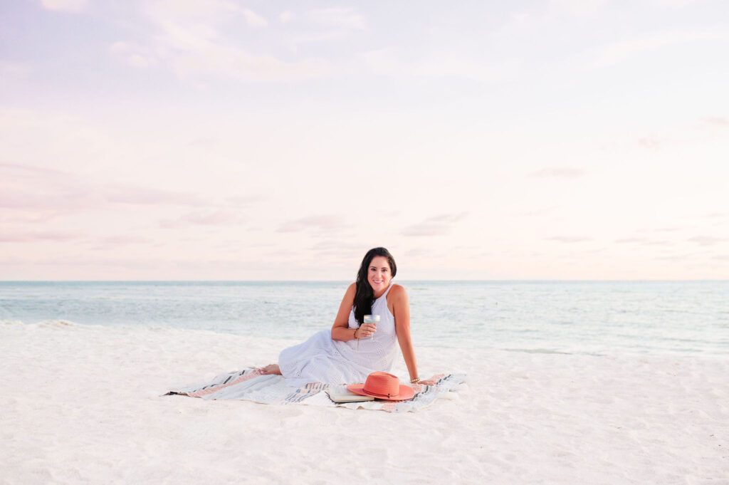 brand photo of life coach sitting at the Lido beach on the blanket and drinking a champagne