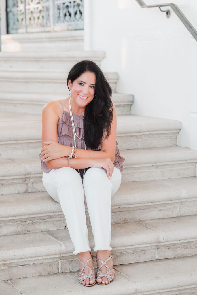 personal branding image of dark hair women looking straight into camera siting at the stairs wearing white pants and dusty pink top