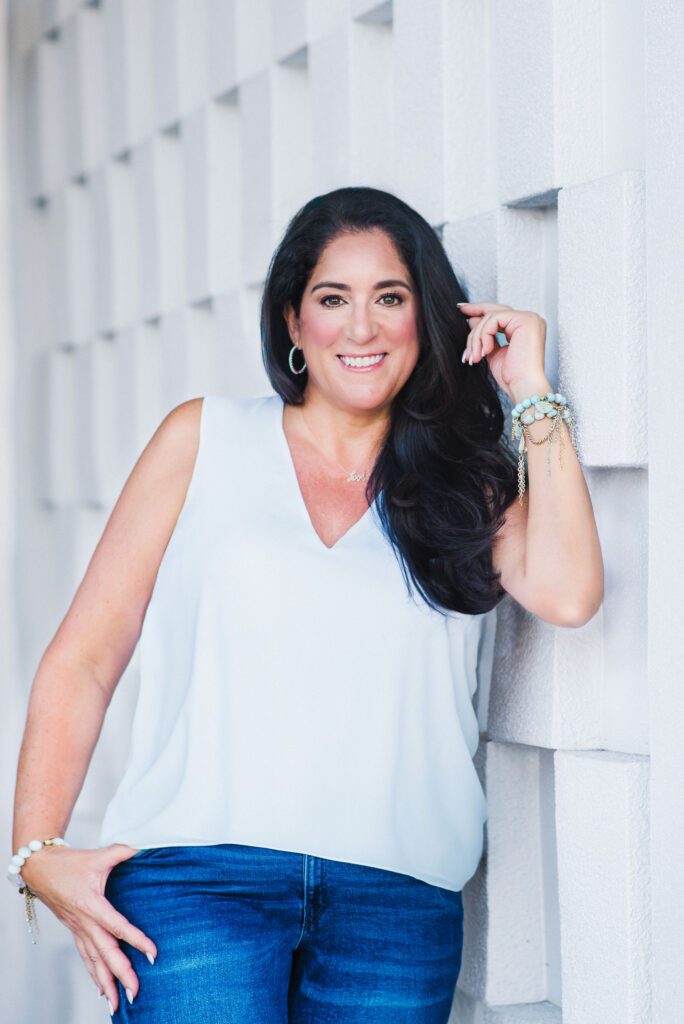 Lifestyle Headshot of dark hair coach wearing white top smiling and leaning turds the camera