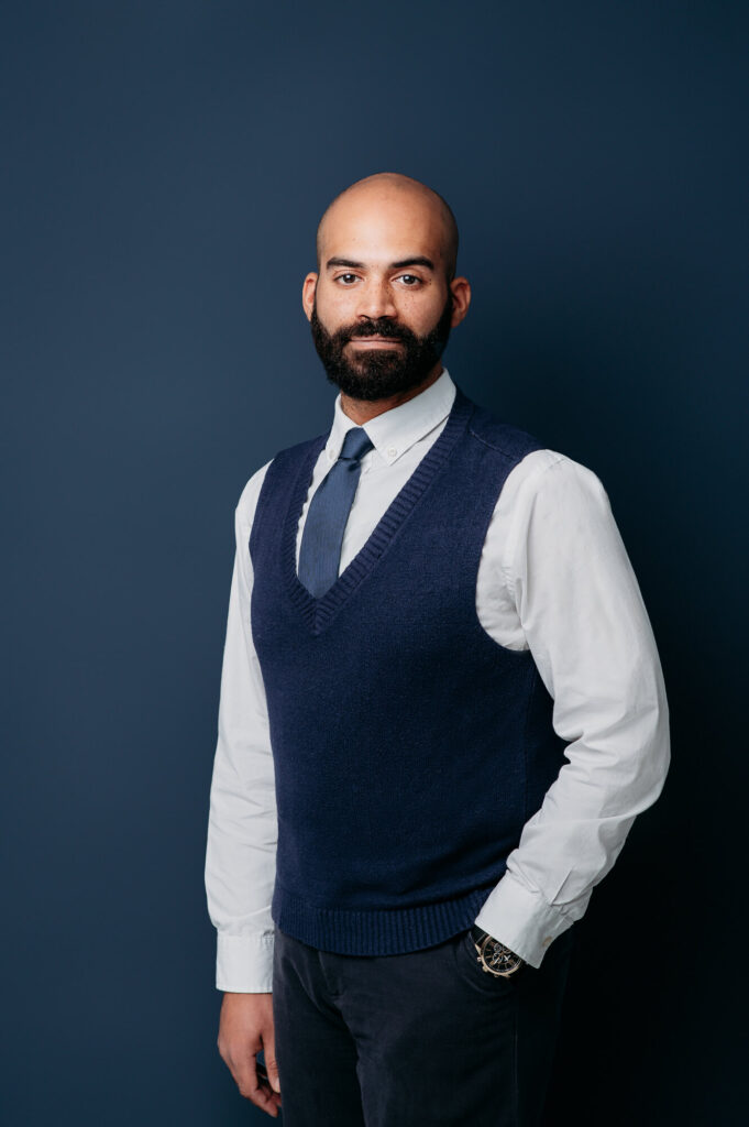 Commercial Headshot of men wearing white shirt and blue vest on dark blue background