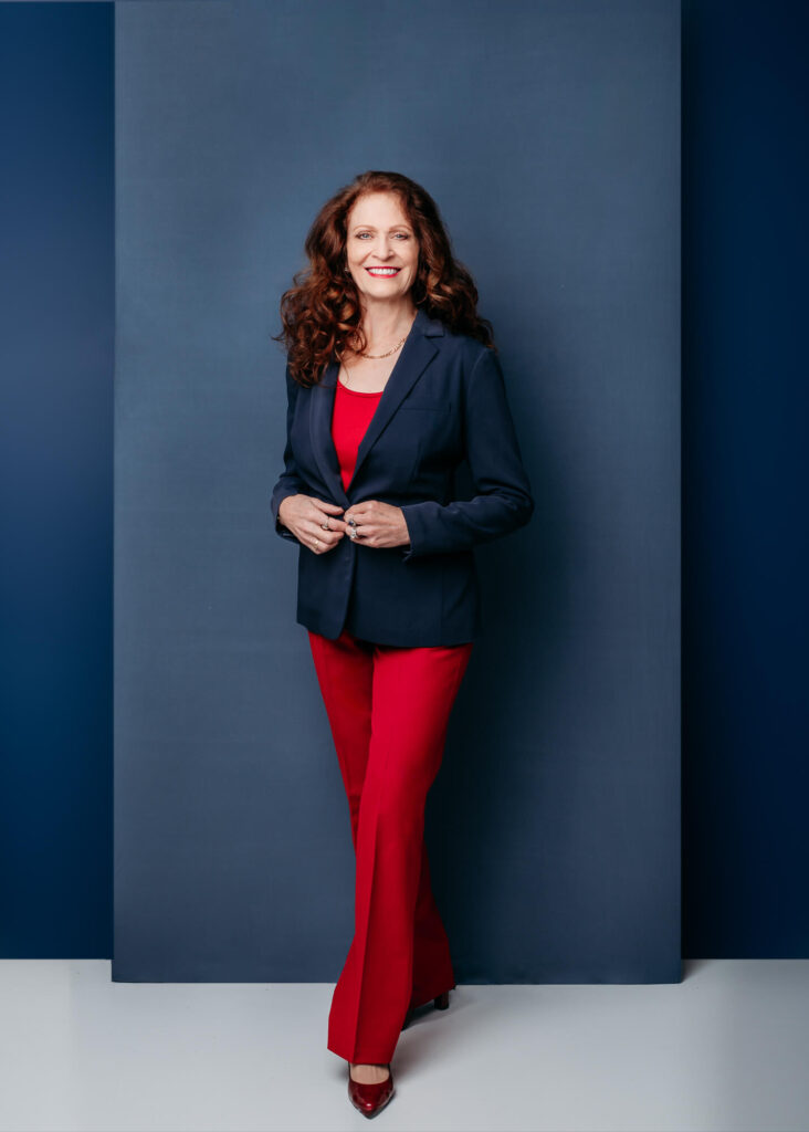 Commercial portrait of dark hair women standing agains blue wall in red pants and dark blue blezer