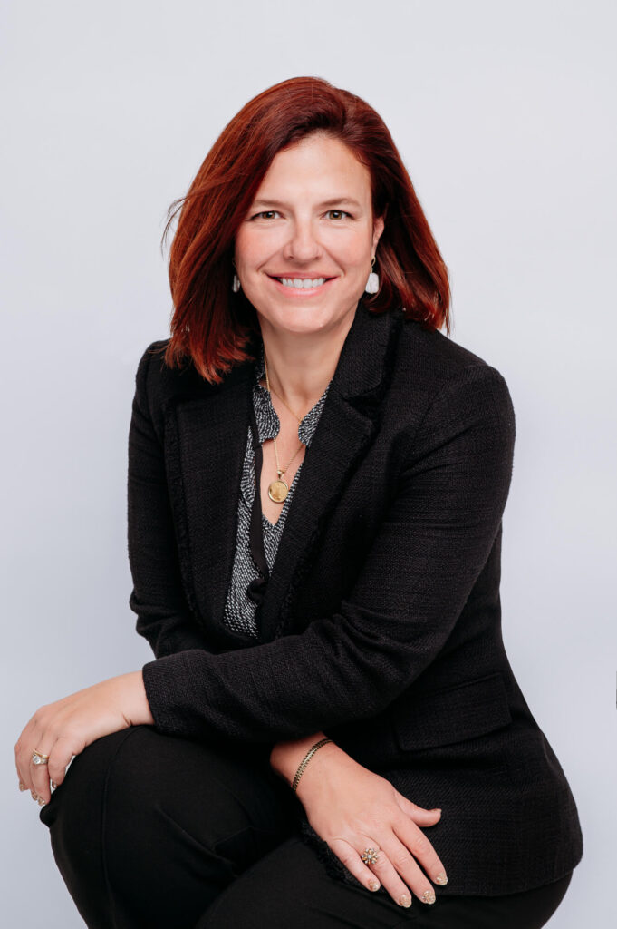 Commercial headshot of women smiling into camera sitting in dark jacket