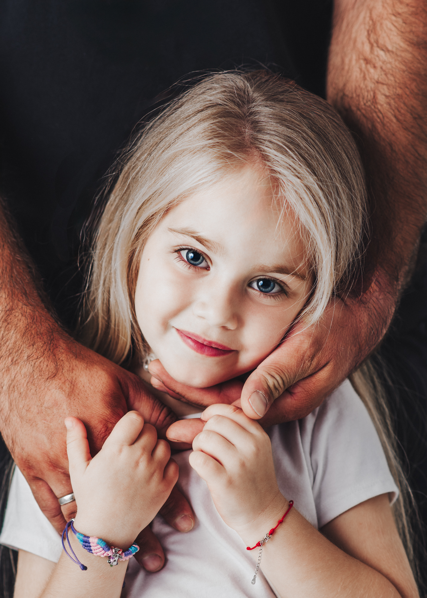 portrait of a little girls looking at the camera holding her father hands